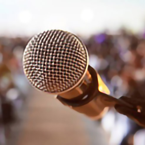 Mikrofon im Vordergrund mit unscharfem Publikum im Hintergrund. Symbolbild für Kontaktinformationen für Medienanfragen bei Amgen.